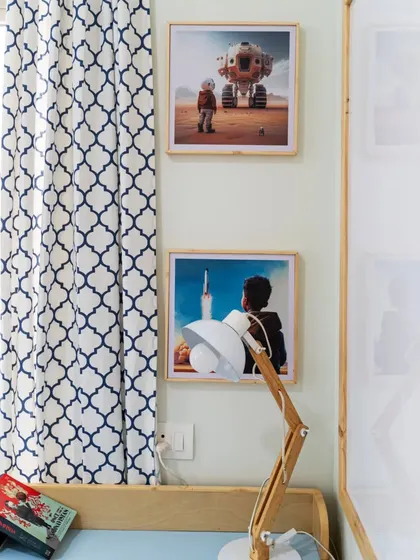 A detail from the space-themed kid's room, showing the curated artwork and a modern wooden lamp on the study desk. The patterned curtains add a touch of geometric style.