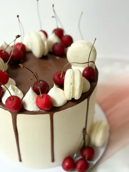 A close-up detail of the cherry and macaron drip cake, showing the texture of the buttercream and the fresh fruit.