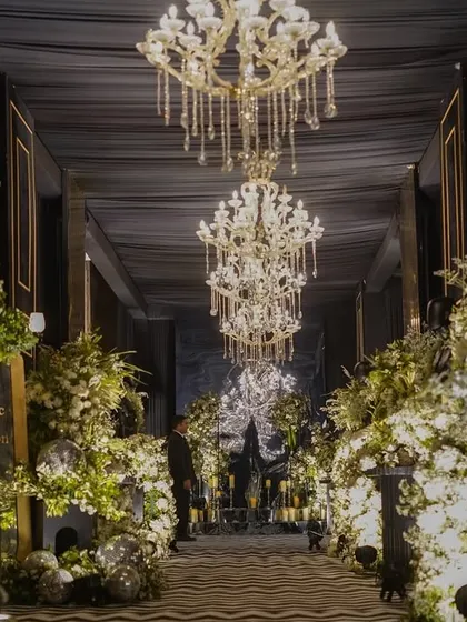 For a modern Sangeet, we designed this dramatic black luxe entrance. The combination of deep, dark drapes, grand chandeliers, and abundant white florals creates a sophisticated and moody atmosphere, promising a night of glamour and high energy.