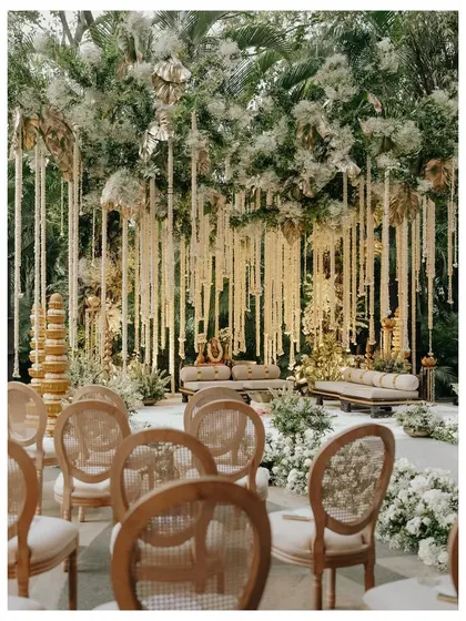A wide shot of the beautiful white floral mandap at The Leela Palace. The image captures the grandeur of the setup, with its cascading flowers and elegant seating arrangement.