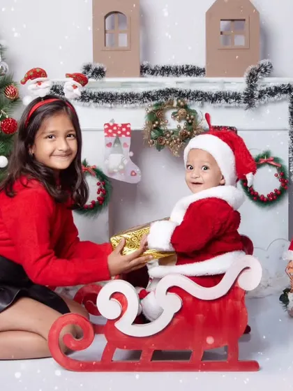 An older sister gives her baby brother a gift as they pose in Santa's sleigh for a magical Christmas photo.
