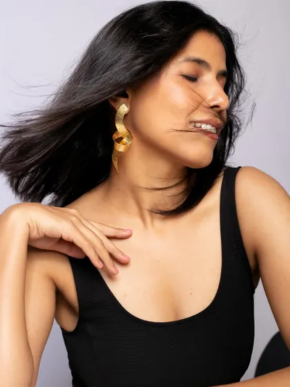 Modeling contemporary wavy gold earrings, this shot uses movement and a gentle smile to bring the piece to life.
