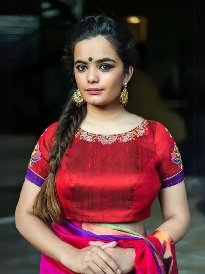 A model wears a bright red blouse with embroidered details, paired with colorful statement earrings.