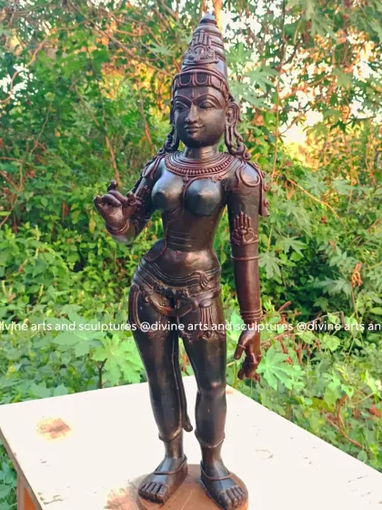 A wax model of Sivagami, a form of Goddess Parvati, representing love and devotion. The outdoor setting highlights the rich, dark color of the wax and the graceful tribhanga (three-bend) posture of the figure.