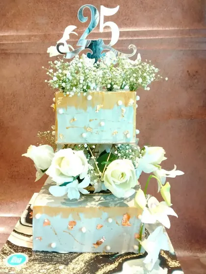 A grand two-tier cake for a 25th anniversary. The design features a silver and gold finish, accented with beautiful white roses and baby's breath for a timeless and celebratory look.