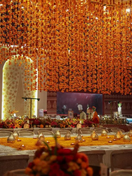 The warm glow of candles on the dining table complements the thousands of hanging marigolds, creating a magical and immersive experience.