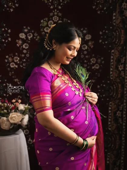 A close up profile shot where she holds a peacock feather to her bump. This artistic composition highlights the beauty of her traditional attire and the precious life she carries.
