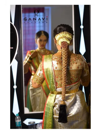 A mirror shot of Rishika, showing the back of her intricately embroidered blouse and her traditional braided hairstyle. Every detail of her look is a reflection of stunning craftsmanship.