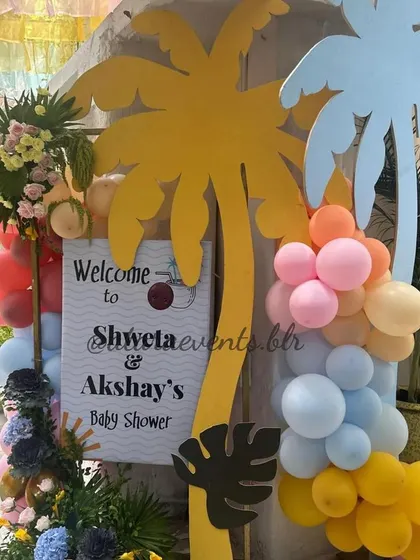 A welcome entrance for a "Coco Baby" shower. The sign is flanked by colorful palm tree cutouts and a lush arrangement of balloons and flowers, creating a vibrant tropical welcome.
