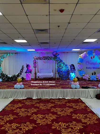 A grand baby shower stage with a floral moon-gate, a traditional jhula, and a balloon ring. The setup is designed to fill a large hall space and create a memorable backdrop for photos.