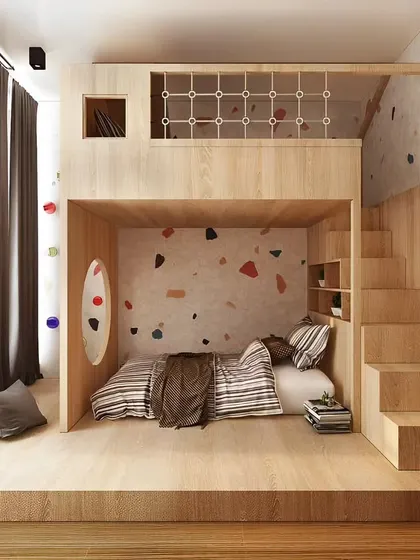 A playful kids' room with a loft bed featuring a terrazzo-patterned accent wall. The design uses natural wood and creates a fun, fort-like sleeping area with storage integrated into the stairs.