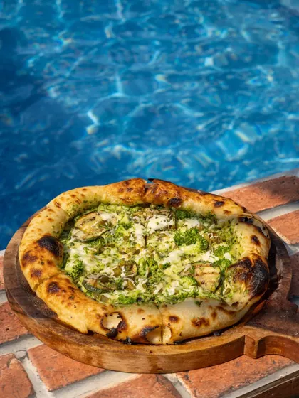 A delicious-looking pizza right by the pool. This shot creates a perfect holiday or vacation vibe, blending delicious food with a relaxed, aspirational setting.