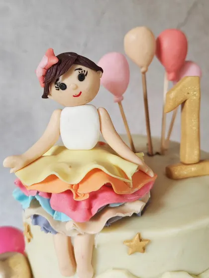 A detailed look at the ballerina topper for a first birthday cake. Her rainbow tutu is made of delicate, individually ruffled fondant layers, and her sweet expression adds a touch of magic.