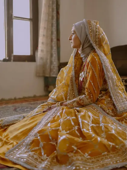 A serene portrait of a Kashmiri Muslim bride, Insha, in her beautiful yellow traditional attire, seated by a window.