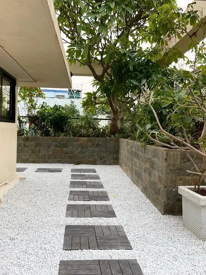 A daytime view of the corporate terrace, highlighting the contrast between the white gravel ground cover and the dark wood stepping stones. The mature trees in the planters provide shade and a sense of establishment.