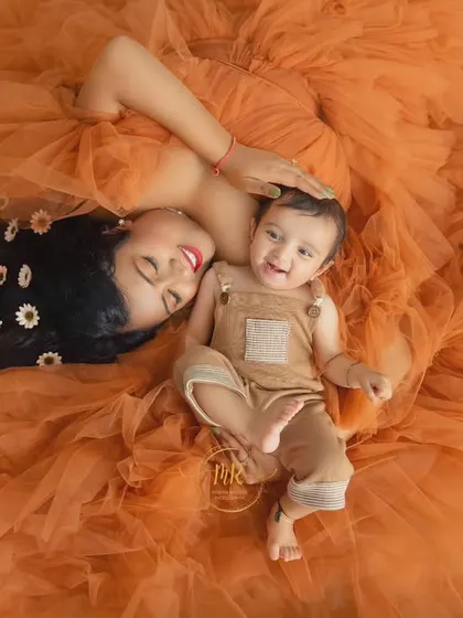 A top-down shot from the same session, with the mother and baby lying on the expansive orange gown, decorated with daisies for a sweet, playful touch.