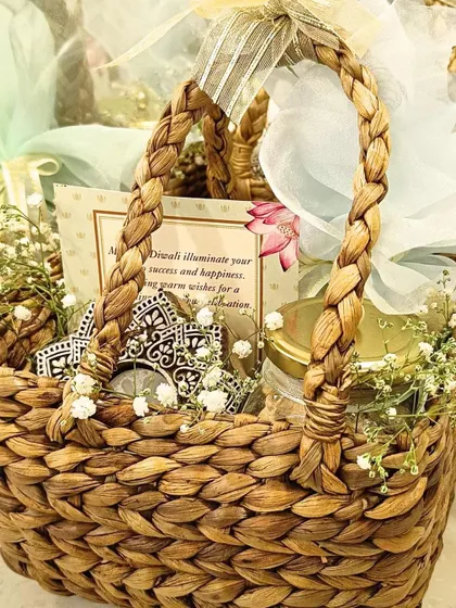 A beautiful and traditional Diwali hamper in a woven hyacinth basket. It includes a jar of goodies, decorative elements, and a personalized card, exuding rustic charm.