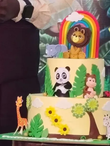A two-tier jungle animal themed cake with fondant figures of a lion, panda, monkey, and other animals.