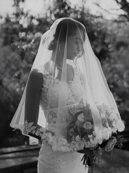 A timeless black and white portrait of a bride in her veil, holding her bouquet. The soft, natural light and her serene expression give this image an ethereal and classic beauty.