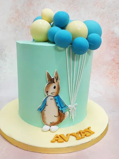 We bring a classic tale to the party with this charming Peter Rabbit cake. The beloved character is featured on a soft, mint-green tier, holding a large bouquet of blue and white balloons, creating a whimsical and gentle design for a first birthday or baby shower.