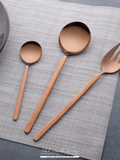 A minimalist shot of copper-toned serving spoons on a simple grey placemat. This composition focuses on the sleek, modern design and elegant lines of the cutlery.