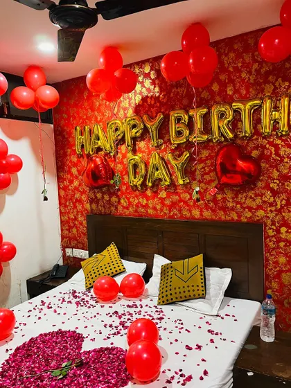 A wider view of the red and gold themed birthday room, showing the bed scattered with rose petals and balloons filling the space for a festive and romantic feel.