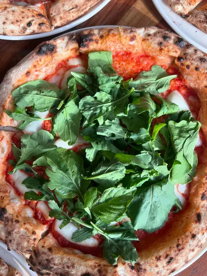 A beautiful pizza topped with fresh arugula and basil. A light and refreshing option.