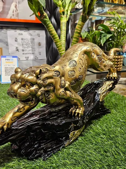 The pouncing jaguar showpiece displayed on a patch of green, highlighting its dynamic pose and antique gold finish.