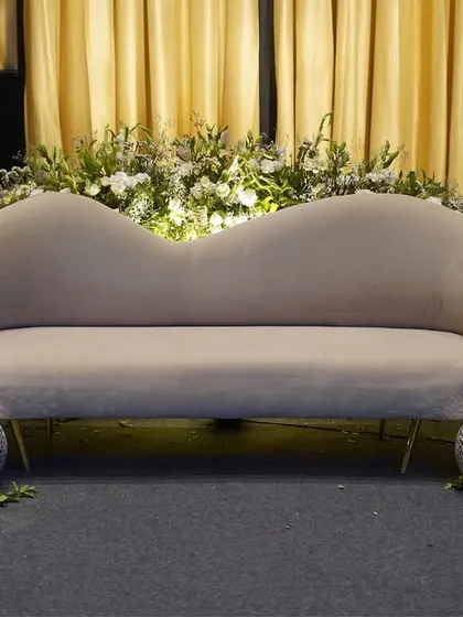 A fun and glamorous photo spot. A modern, curved sofa is surrounded by an abundance of white flowers and sparkling disco balls, perfect for a party atmosphere.