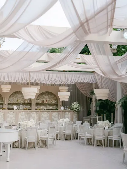 A wide view of the "Ivory Dreamscape" event, showing the interplay of the draped ceiling, modern chandeliers, and all-white decor. The white piano adds a final touch of classic elegance.