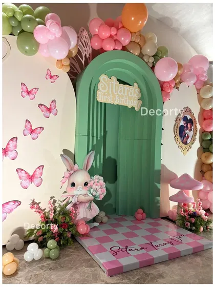 A close-up of the 'Alice in Wonderland' backdrop, featuring a checkered floor, bunny prop, and butterfly details.