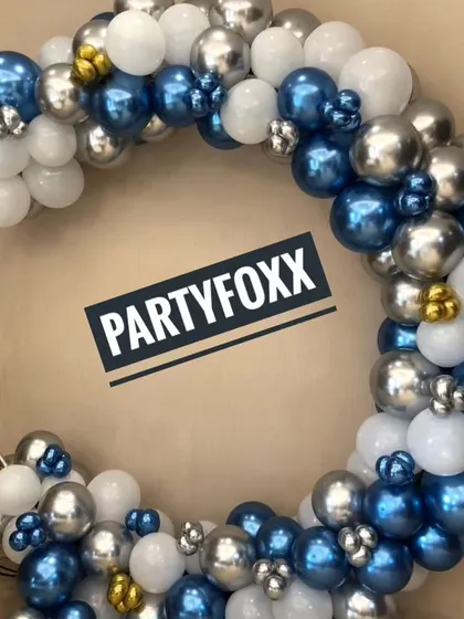 A stylish circular balloon arrangement in metallic blue, silver, and white, perfect for a modern and sophisticated adult party or corporate event.