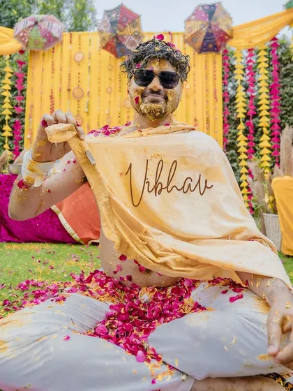 A cool and candid portrait of the groom after being completely covered in turmeric and flower petals. His sunglasses and relaxed pose add a fun and memorable touch to the haldi photos.