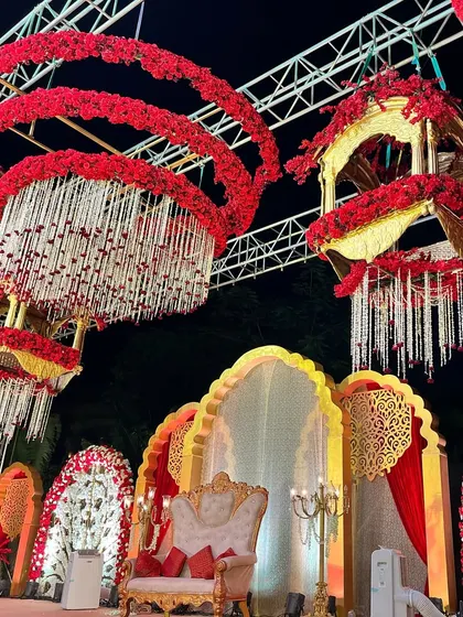 A closer look at the stunning hanging decor elements. These custom-made chandeliers, adorned with red flowers and white floral strings, add a unique and grand touch to the wedding stage.