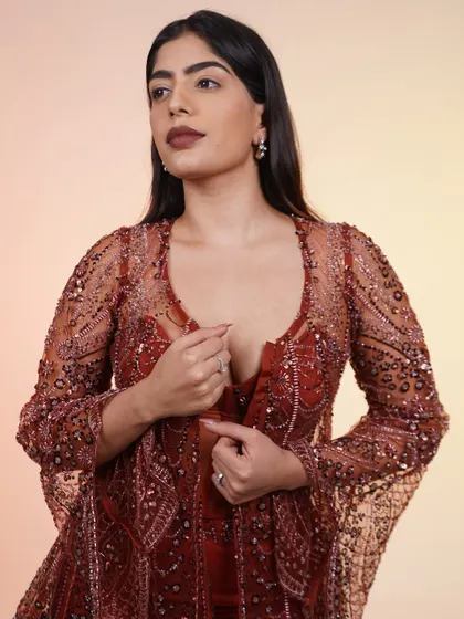 A full-length shot of the rust-colored corset set. The sheer jacket and corset top create a look that is both edgy and elegant.