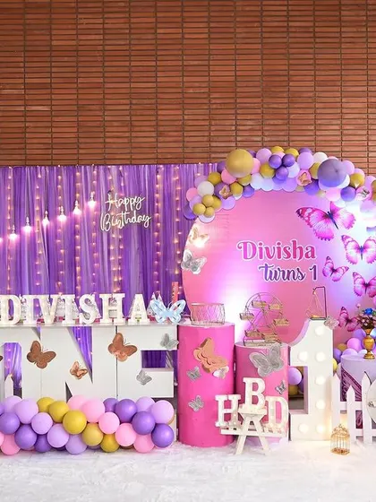 A vibrant butterfly-themed decor in purple and pink. This setup includes a circular backdrop, a "Happy Birthday" neon sign, and large butterfly cutouts to make the stage pop.