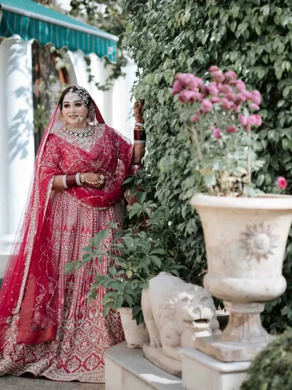 A classic bridal portrait. The bride, in her beautiful red lehenga, poses gracefully in a garden setting, creating a timeless and elegant image.