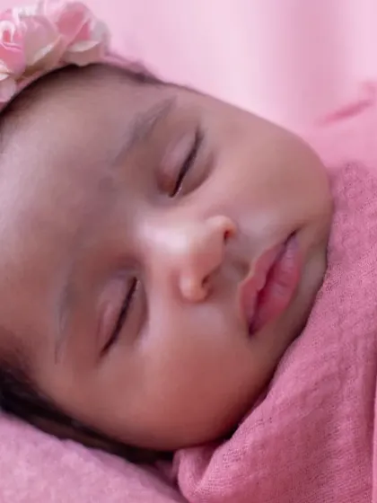 A close-up portrait of a newborn wrapped snugly in a pink swaddle, her peaceful, sleeping face the center of attention.