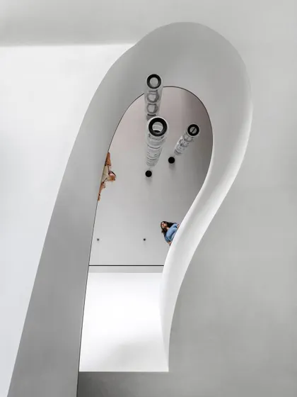 Looking down into the void of the sculptural staircase, the form appears like a ribbon of light. The design is not just about moving between floors, but about creating a powerful visual and spatial experience.