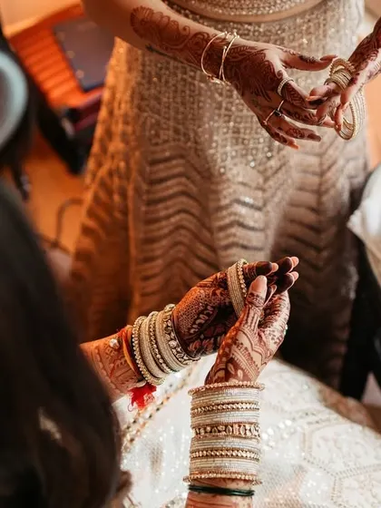 A close-up shot of the bride's hands as she puts on her bangles, a classic getting-ready moment full of anticipation.