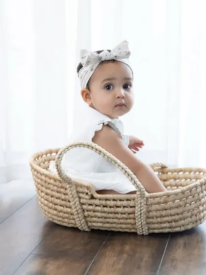 A beautiful baby girl sitting in a woven basket. The clean, bright background makes her sweet expression the complete focus.