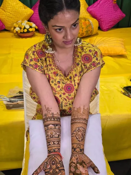 A lovely bride showcasing her full-arm mehandi. The design features a mix of personalized cityscapes and traditional patterns, creating a unique and beautiful bridal look.