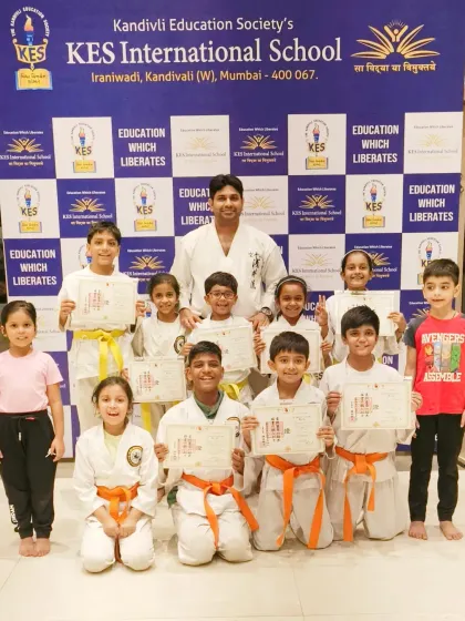 A full group photo from the belt distribution at KES International School, showing students from beginner to intermediate levels.