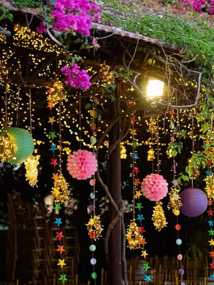 An evening view of the colorful hanging decor, illuminated by fairy lights. The bougainvillea flowers on the roof add another layer of natural beauty to the festive setup.