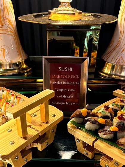 A beautifully arranged sushi station with a variety of rolls and nigiri. The menu lists options like Teriyaki Chicken Katsu and Asparagus Tempura, showcasing the customizable nature of our offerings.