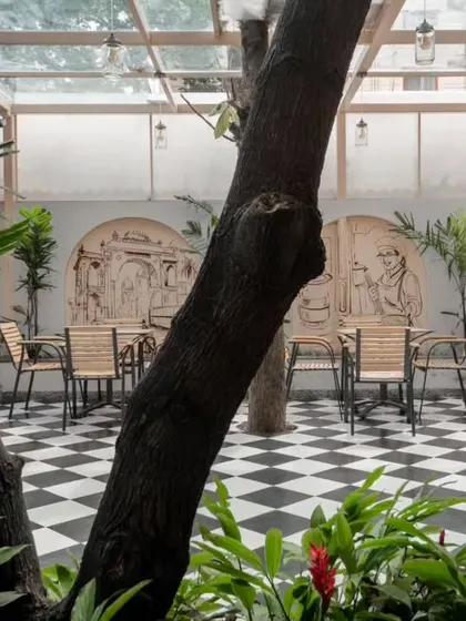 A view through the foliage into the outdoor dining courtyard. The design prioritizes the preservation of trees, which become natural columns and canopies for the space.