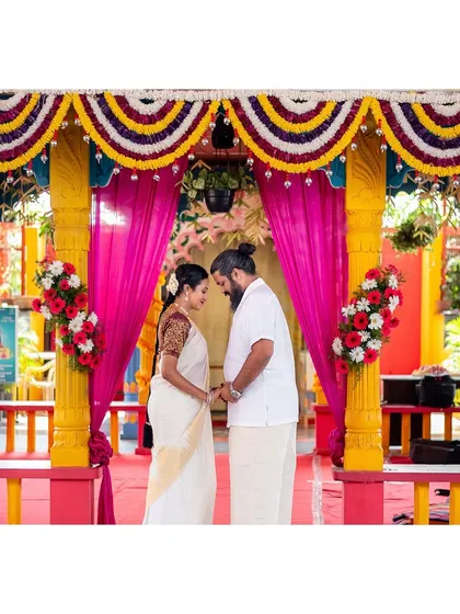 A couple stands together under a brightly decorated mandap, sharing a quiet moment before a ritual.