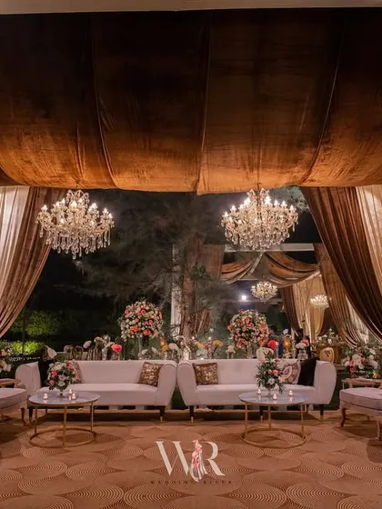 A full view of a lounge area designed for a sophisticated engagement. The space is defined by a patterned floor, plush white seating, and a canopy of brown and cream drapes, creating a perfect balance of comfort and style.