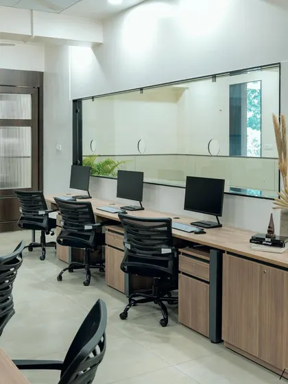 In this office design, a large internal window provides a visual connection to an adjacent area, bringing in more light. The workstations are kept clean and organized, with simple decor like dried pampas grass to add a touch of warmth.