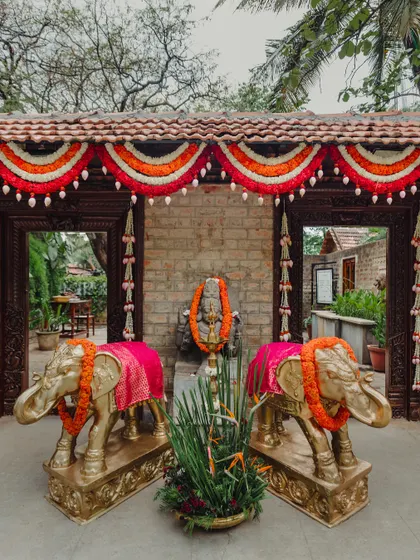 Golden elephant statues draped in pink fabric and marigold garlands, standing guard at the entrance to a ceremony.